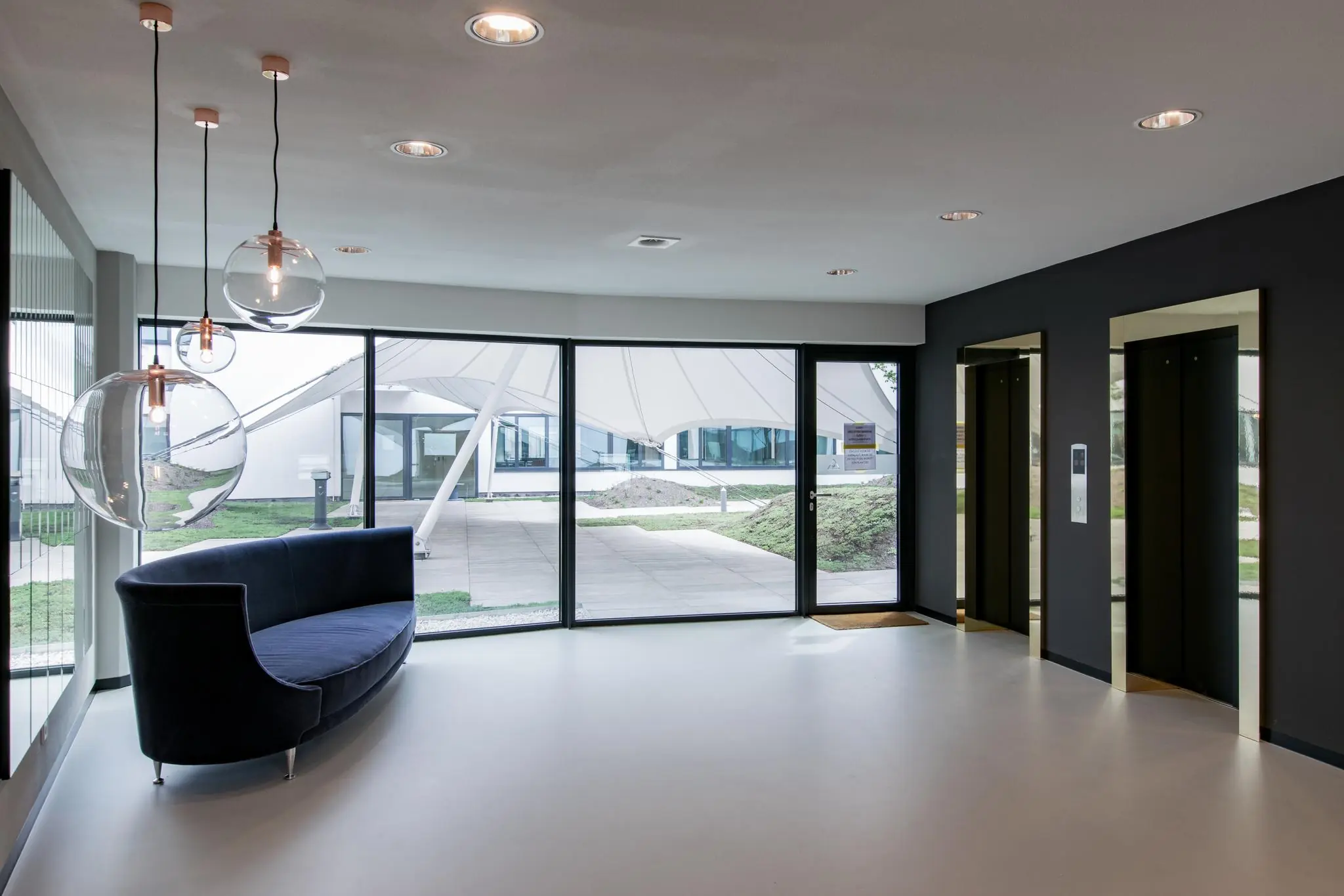 Moderne lobby van een kantoorgebouw aan de Grote Marktstraat met glazen hanglampen, een donkerblauwe bank en twee liften.